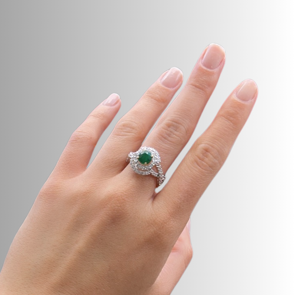 A close-up of a hand wearing a silver ring with a round green gemstone and small clear accent stones, set against a soft gray gradient background.